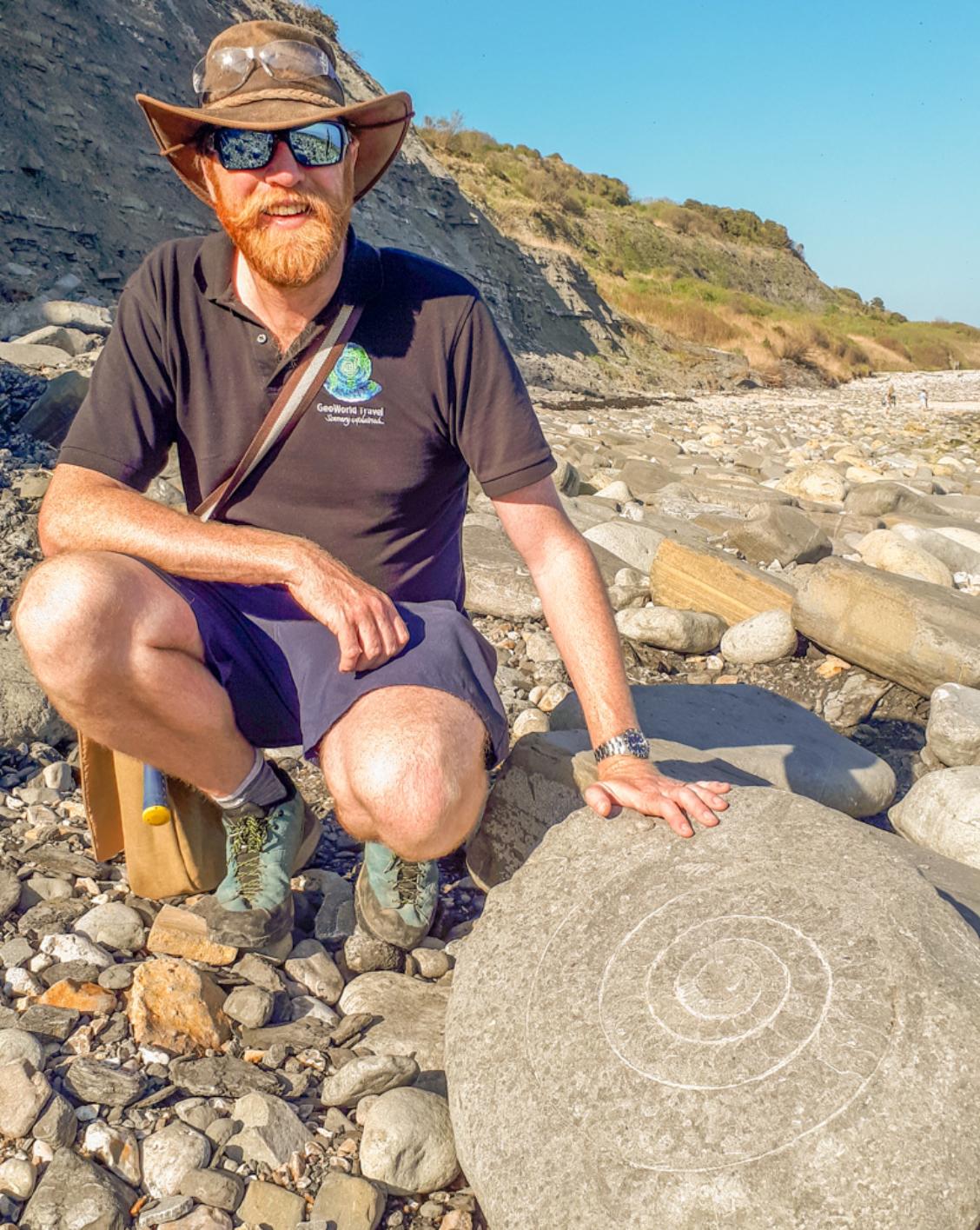 A photograph of James Cresswell with an ammonite fossil on Jurassic Coast at Lyme Regis