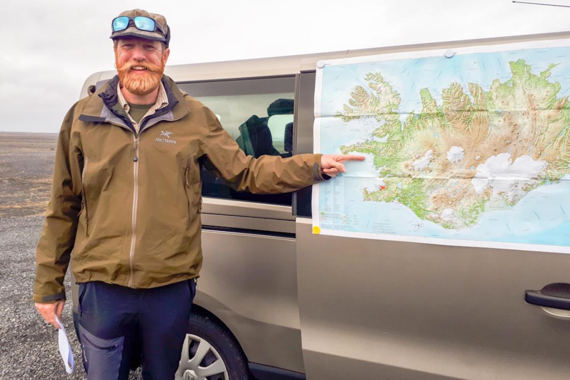 A photograph of James Cresswell pointing to a map of Iceland while leading a geology tour